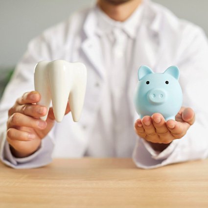 Man in white coat holding model tooth and blue piggy bank