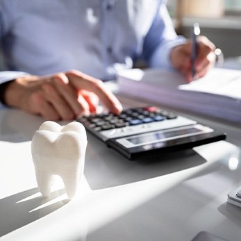 Someone working with pen, paper, and calculator at desk with model tooth