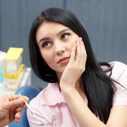 Concerned woman in dental chair rubbing jaw in pain