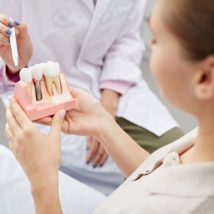 Dental patient holding dental implant model that dentist is pointing to