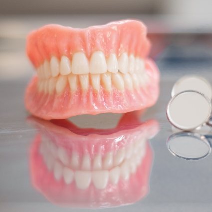 Full dentures in Rogers on reflective surface next to dental mirror