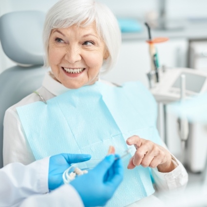 Senior woman smiling at dentist holding denture