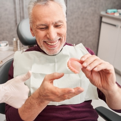 Smiling male dental patient holding a denture