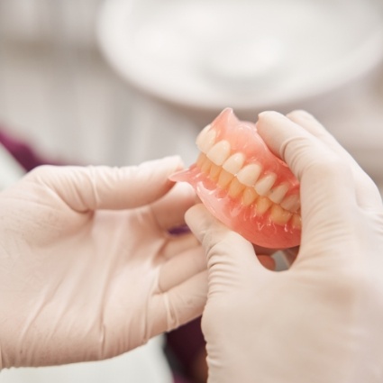 Gloved hands holding pair of full dentures