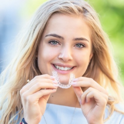 Woman with blonde hair putting in Invisalign clear aligner in Rogers