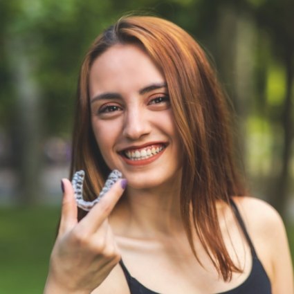 Red haired woman smiling and holding Invisalign aligner