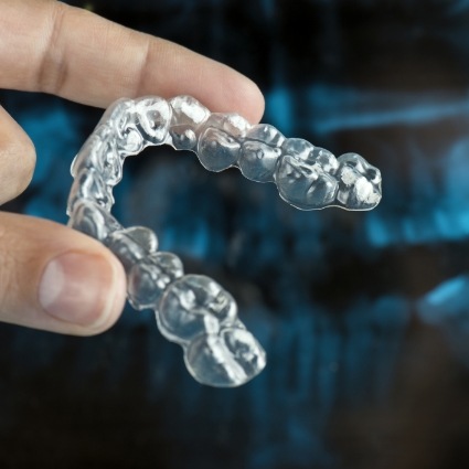 Hand holding Invisalign aligner between two fingers