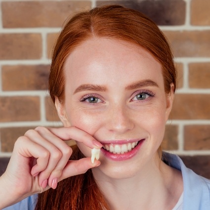 Close up of smiling red haired woman holding a tooth