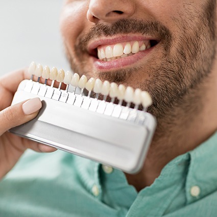 Man in green shirt smiling while dentist holds shade guide to his teeth