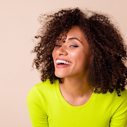 Woman with curly brown hair in chartreuse shirt smiling with tan background