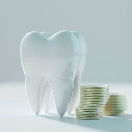 Large model tooth next to pile of coins on a white surface