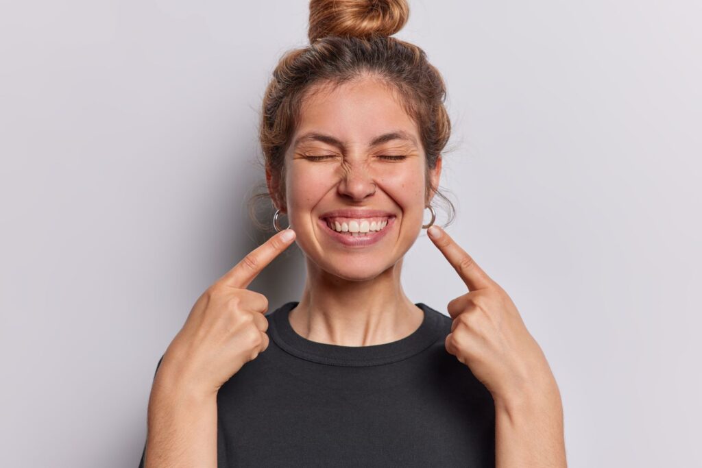 A woman smiling and pointing to her healthy teeth.